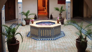 An arched corridor with a tiled floor, potted plants, and a central decorative fountain.