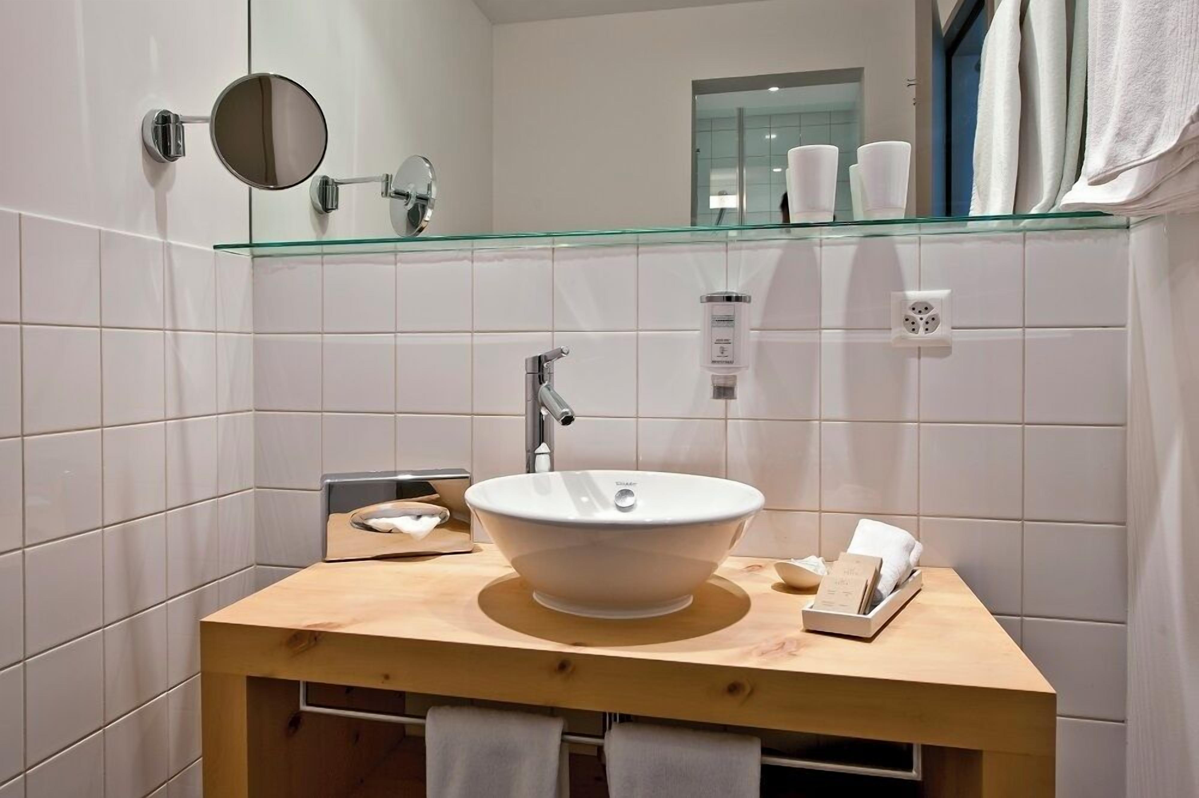 Un baño con un lavamanos tipo cuenco, un espejo y un estante de vidrio sobre el lavamanos.
