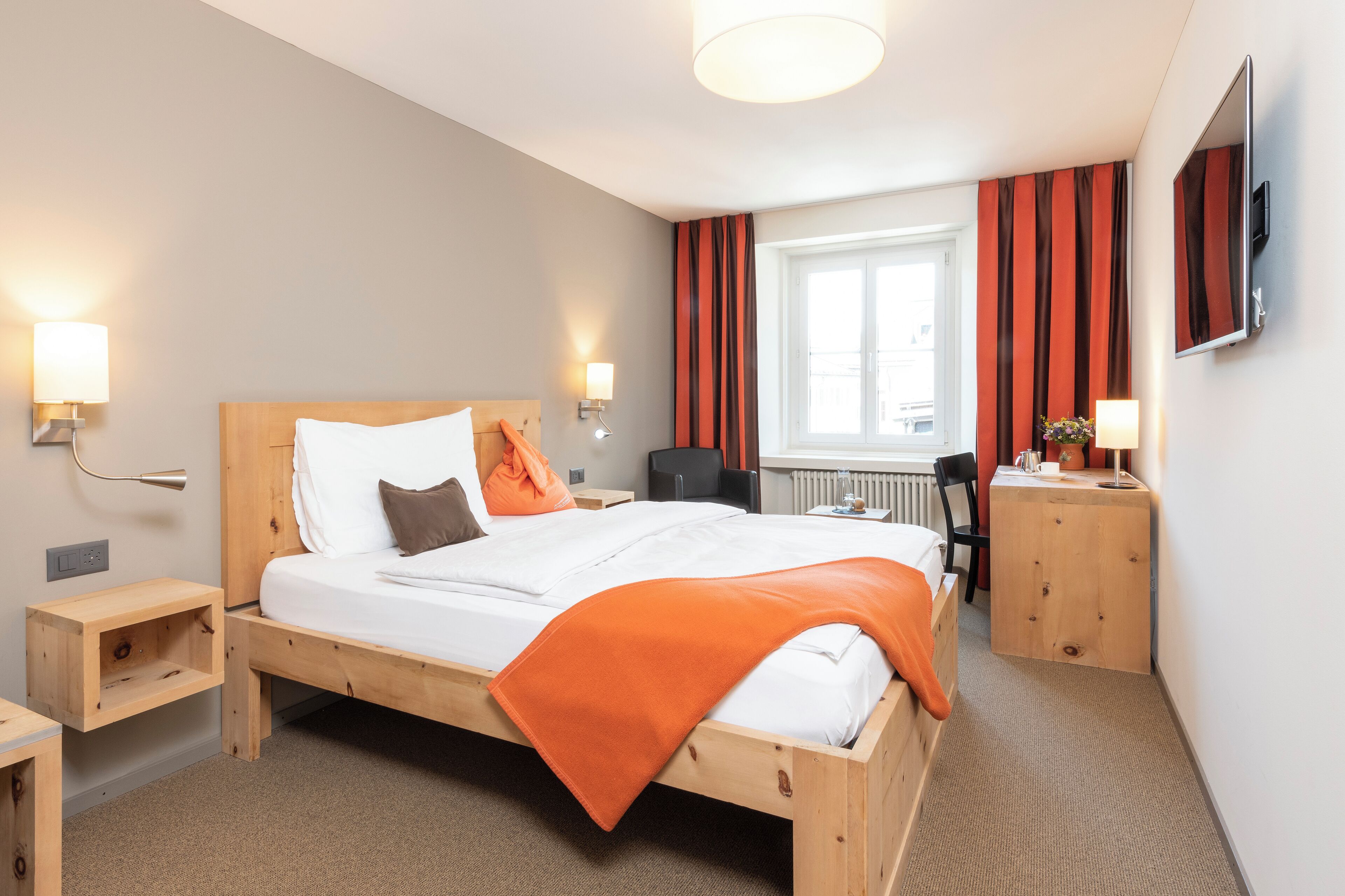 A hotel room with a wooden bed, bedside tables, a desk, and a chair.