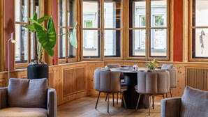 Ein Eckzimmer mit einer holzverkleideten Wand, einem runden Tisch mit Stühlen und einer großen Topfpflanze.