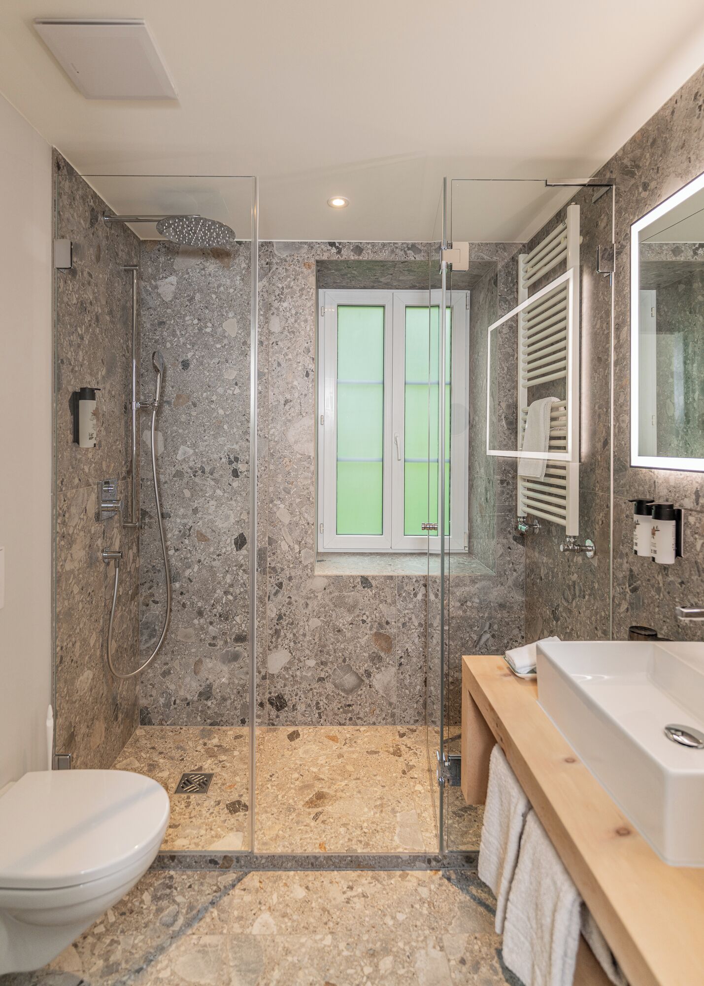 Une salle de bain moderne avec une douche à parois de verre, des toilettes blanches et un meuble-lavabo en bois doté d’un grand miroir.