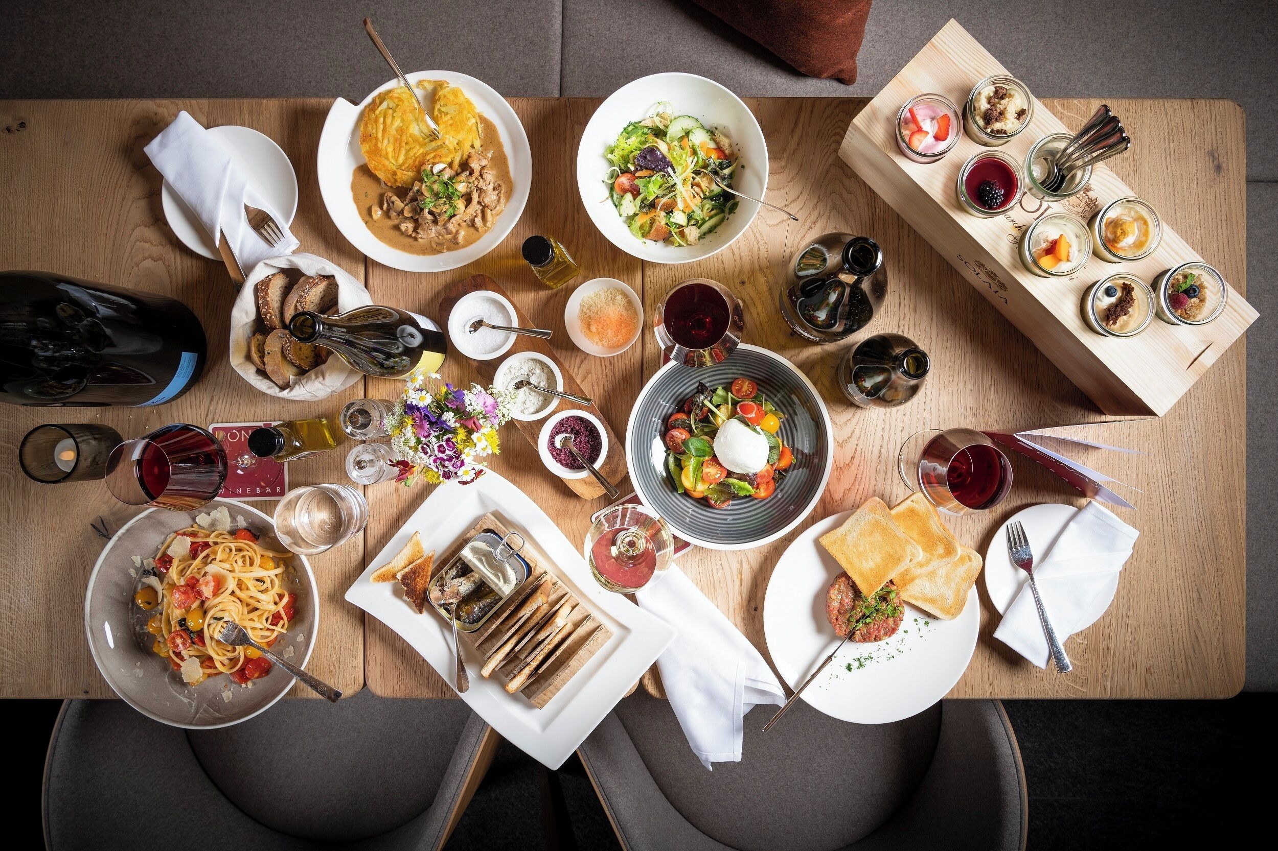 A dining table with various dishes, glasses of wine, and a bottle of wine.