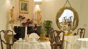Un comedor con manteles blancos, sillas de madera, un espejo con marco dorado y una estatua de una mujer.
