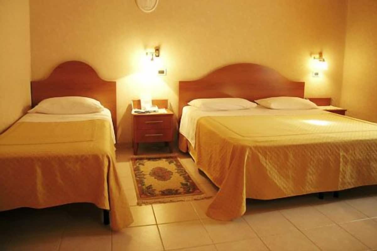 A hotel room with two single beds, a nightstand with a lamp, and a small rug.