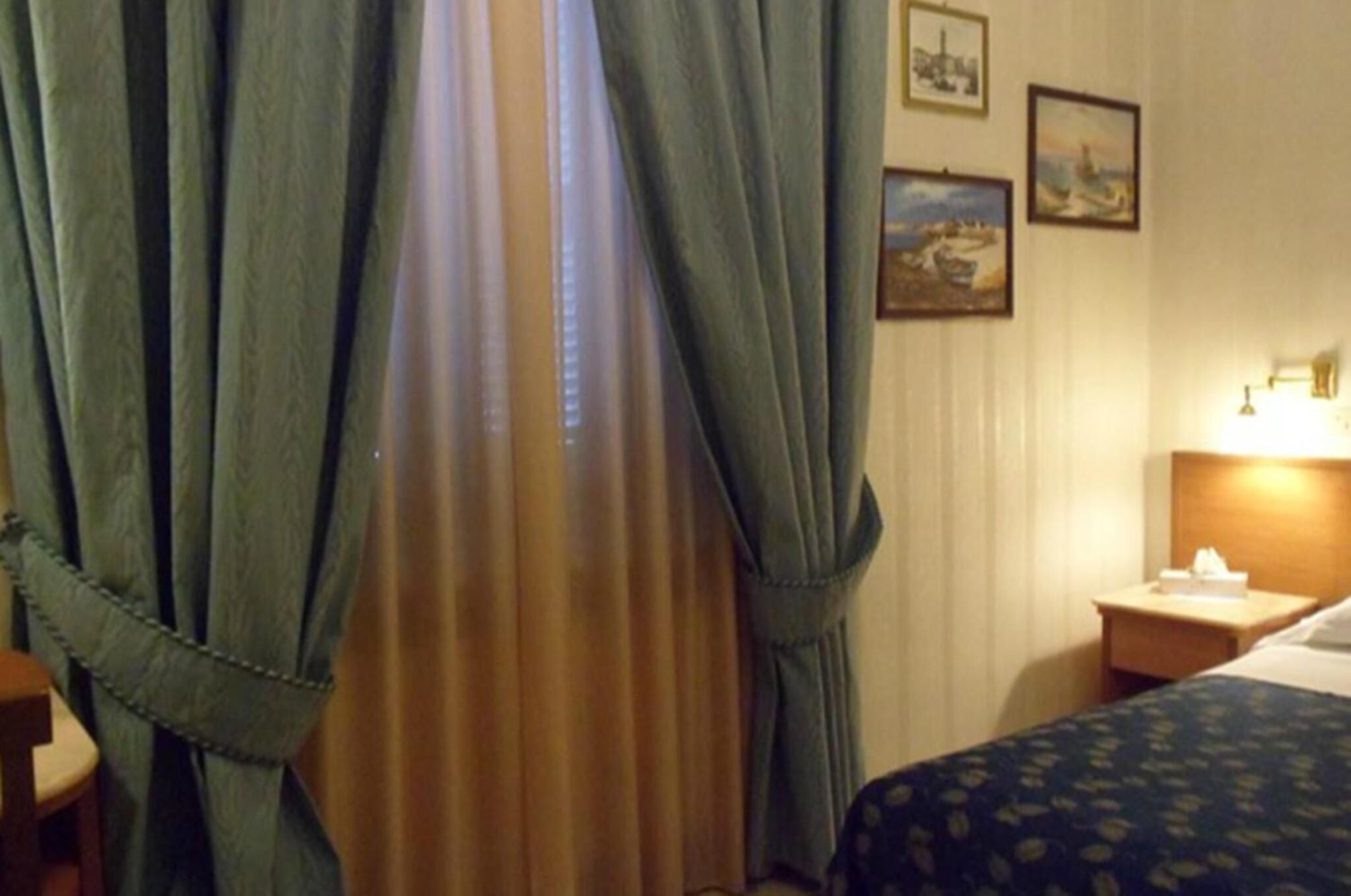 Une chambre d’hôtel avec un lit, une table de chevet, une lampe et des rideaux.