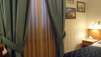 Une chambre d’hôtel avec un lit, une table de chevet, une lampe et des rideaux.