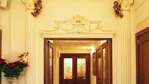 Un pasillo con detalles ornamentales en el techo, una puerta de madera al final y una silla en el centro.