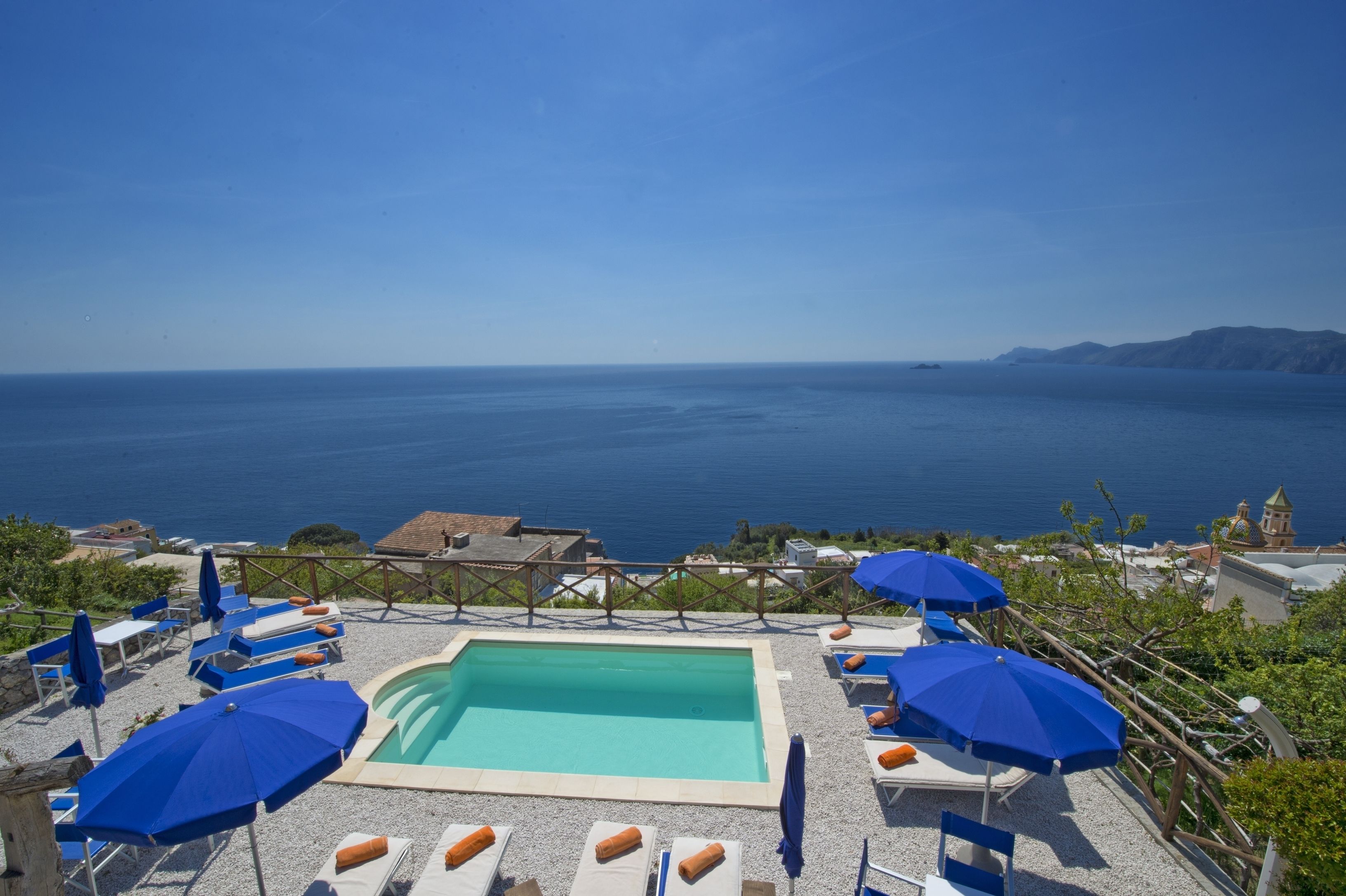 Un espace piscine agrémenté de parasols bleus et de chaises longues, avec vue sur la mer.