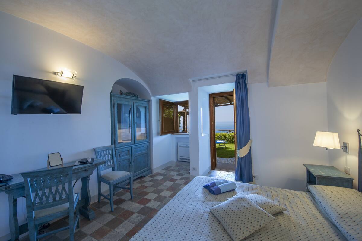 Habitación de hotel con cama, escritorio, silla, televisión y vista al exterior.