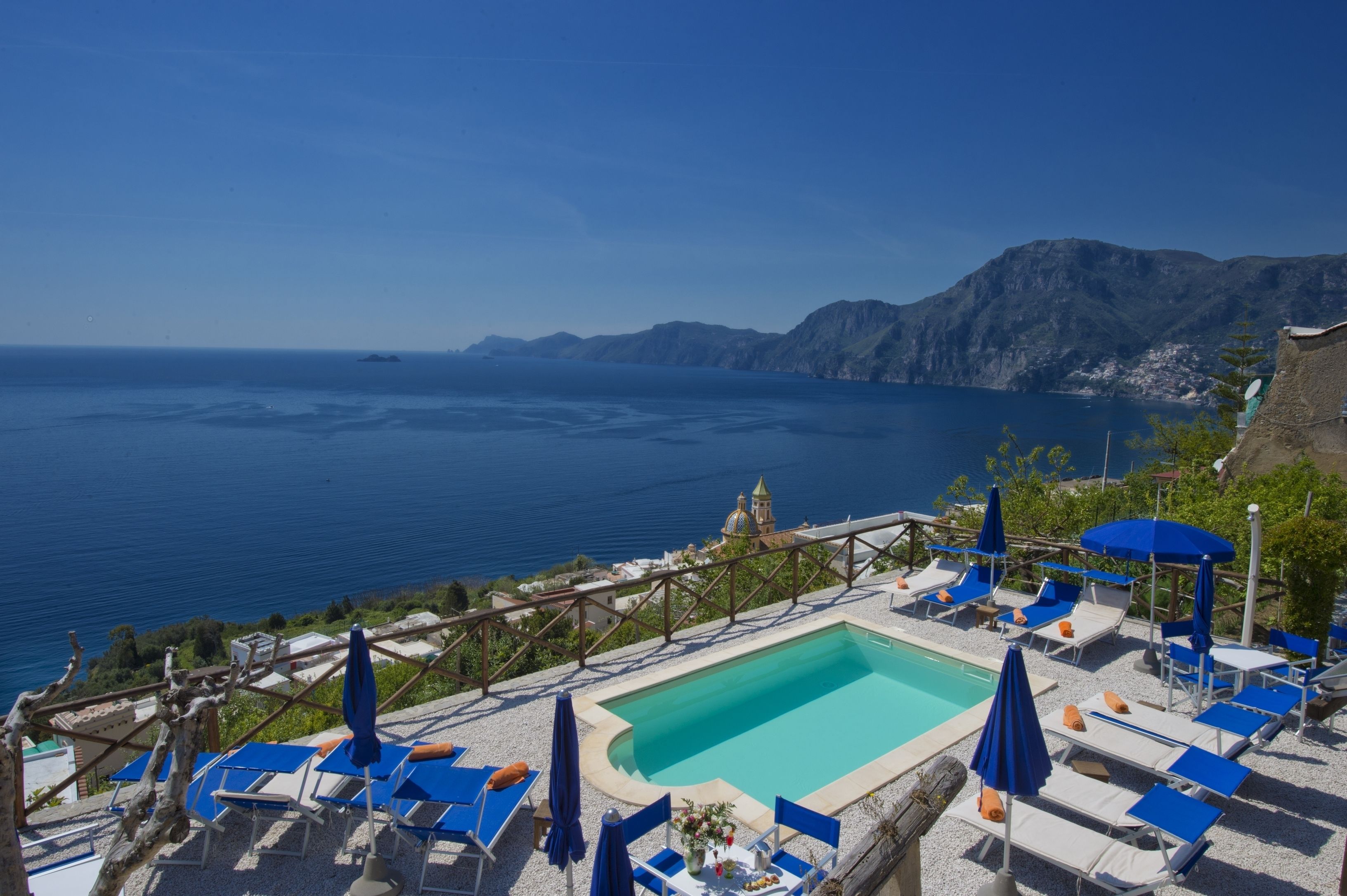 Un espace aménagé au bord de la piscine, avec des chaises longues et des parasols, offrant une vue sur un plan d’eau et des montagnes.