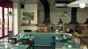 L’intérieur d’un restaurant avec des tables et des chaises vertes, un comptoir de bar et des luminaires suspendus.