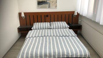 Un dormitorio con cabecera de madera, cama con ropa de cama a rayas, una mesita de noche, una lámpara y un cuadro en la pared.