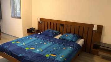 Un dormitori amb un panell de fusta al capçal, dues taules de nit, una cambrera i un llit amb una col·cha i almoines blaves amb estampat floral.