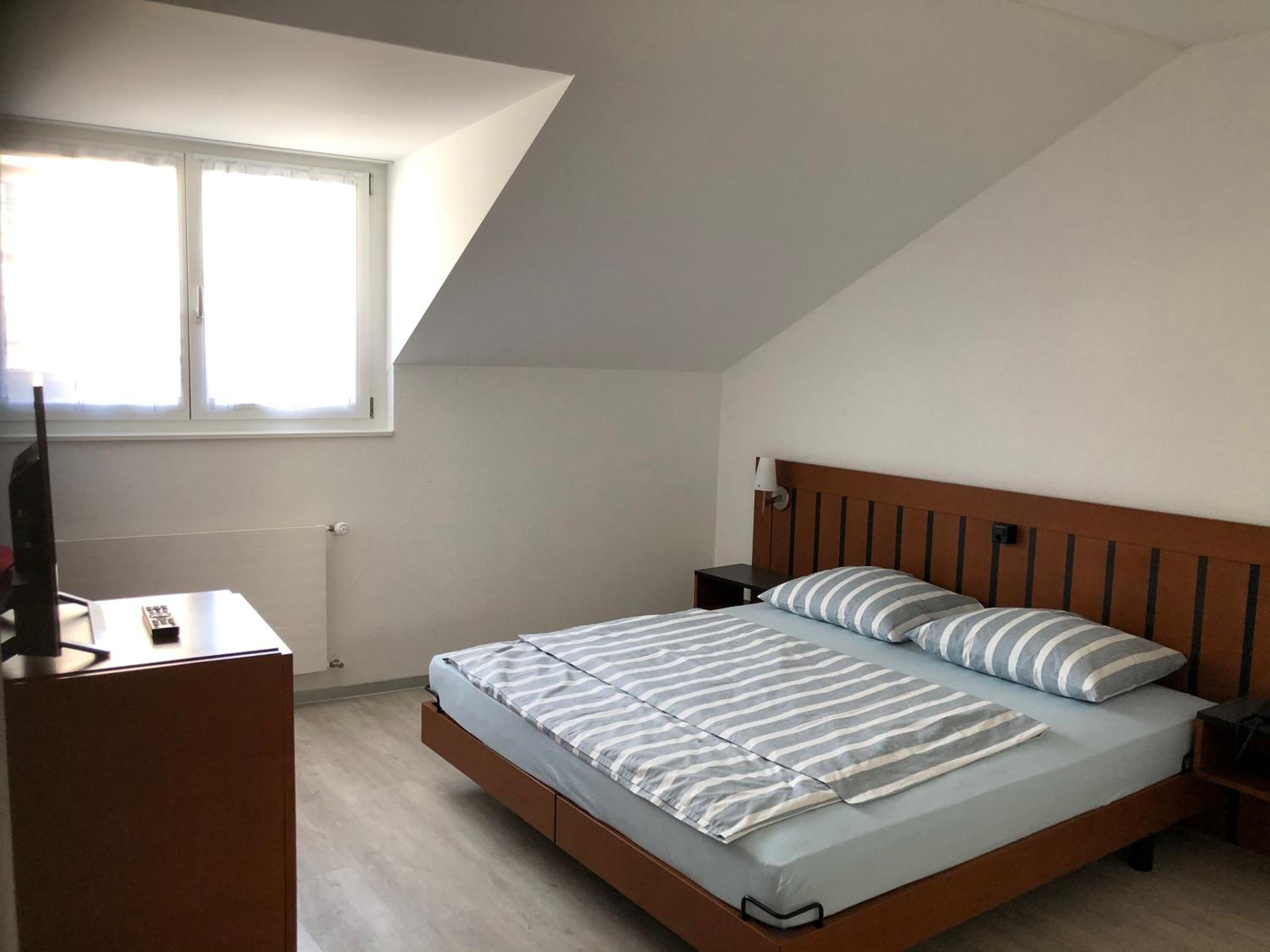 A bedroom with a sloped ceiling, a bed with striped bedding, a bedside table, and a TV on a stand.