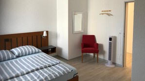 A bedroom with a bed, a red chair, a standing heater, and a mirror on the wall.