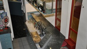A kitchen with a granite countertop, a sink, and a stainless steel range hood. There are red stools and a glass display case with bottles.