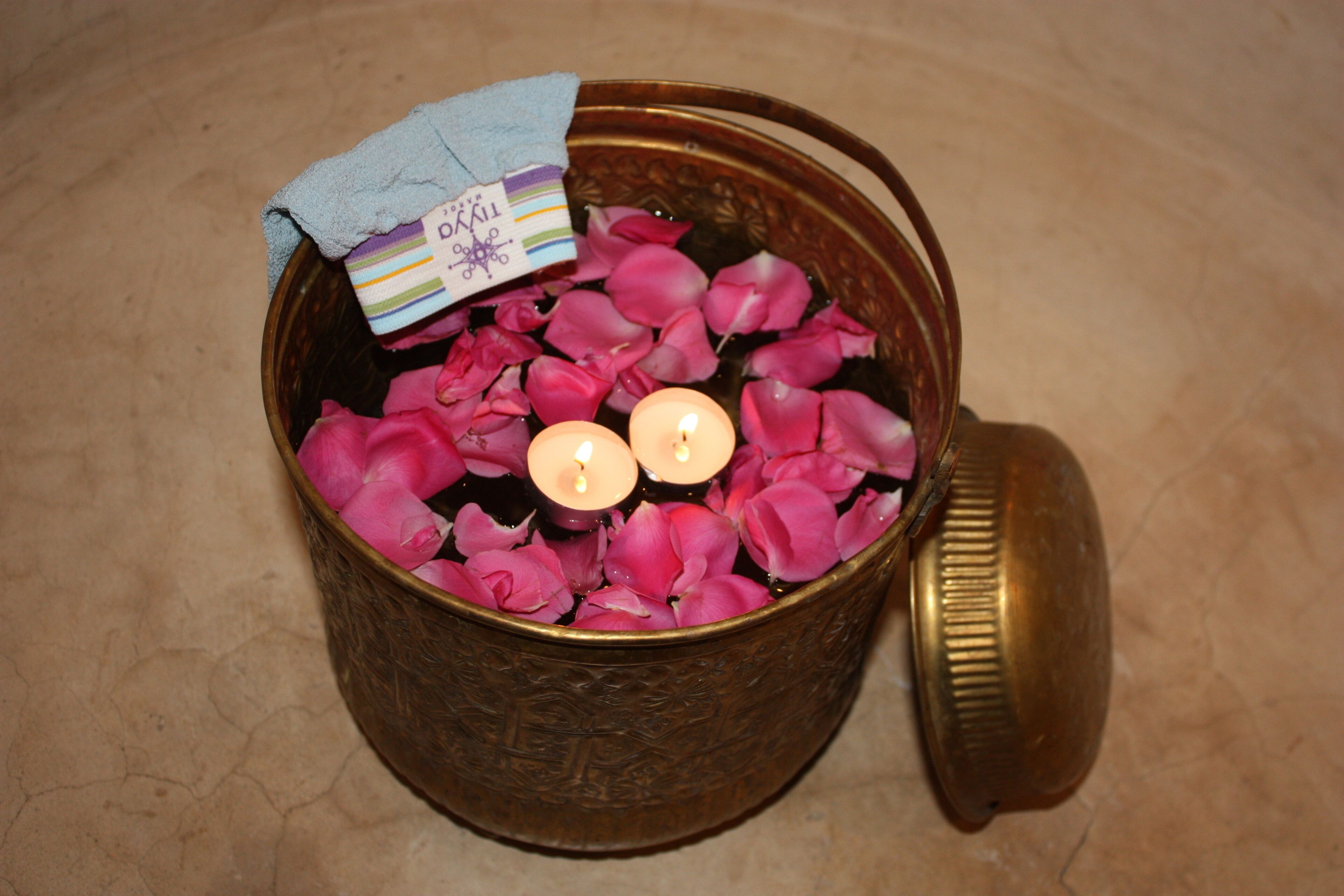 Un cuenco de latón lleno de pétalos de rosa rosados y dos velas encendidas.