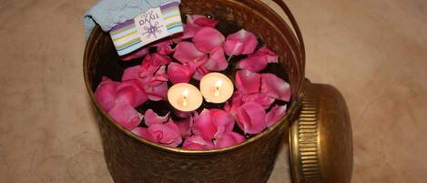 Un cuenco de latón lleno de pétalos de rosa rosados y dos velas encendidas.