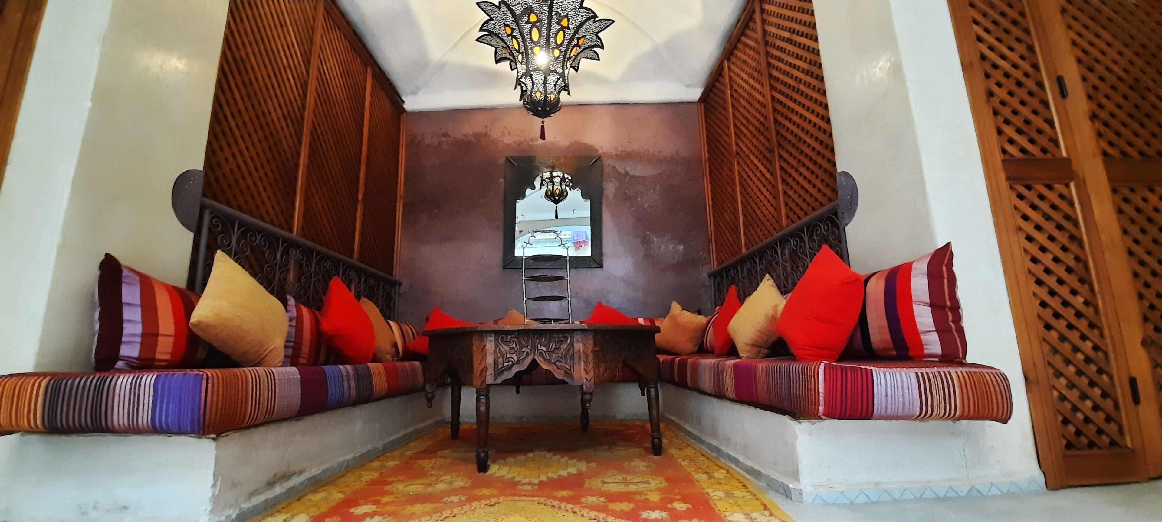 Un interior tradicional marroquí con un banco de madera, cojines coloridos, un tapete estampado y una lámpara decorativa.