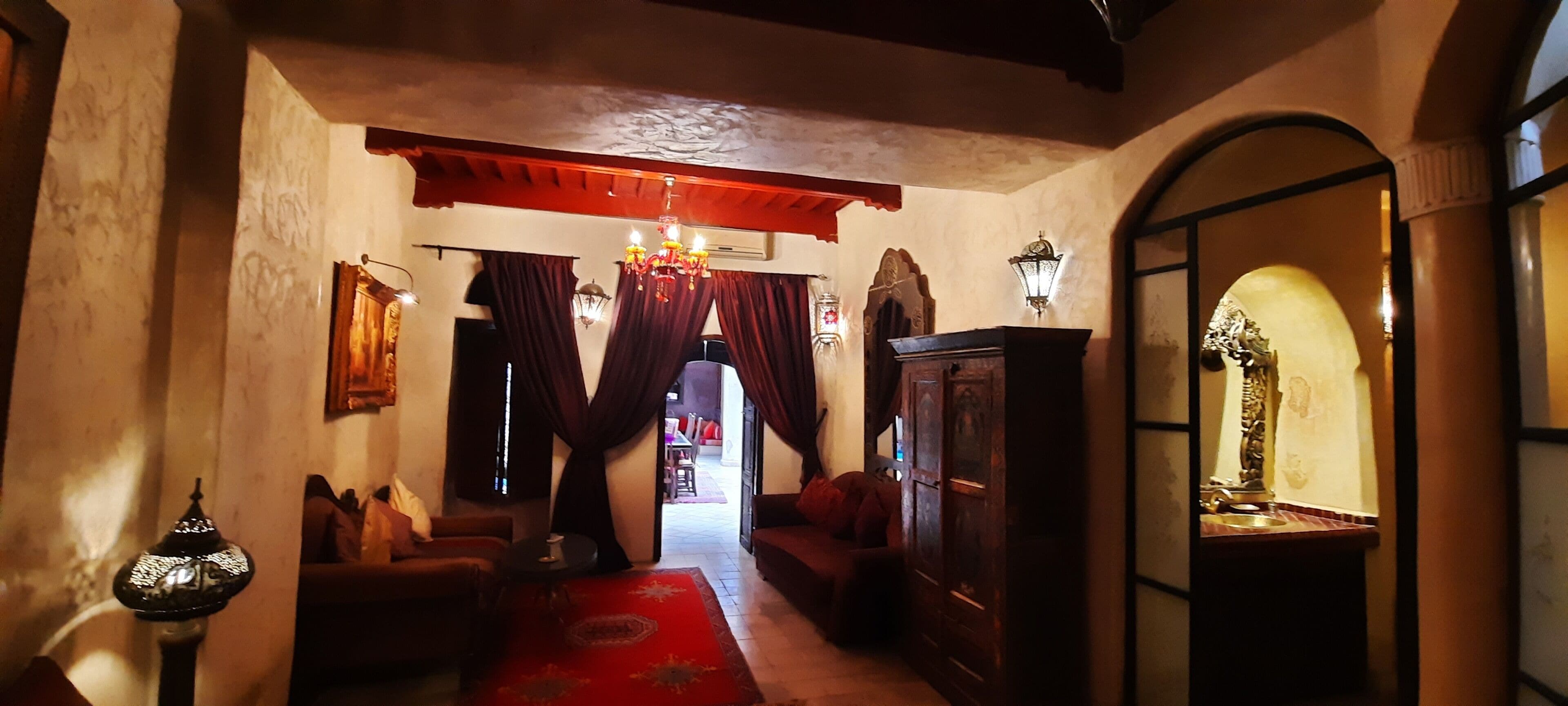 A hallway with a red carpet, wooden furniture, and a chandelier.