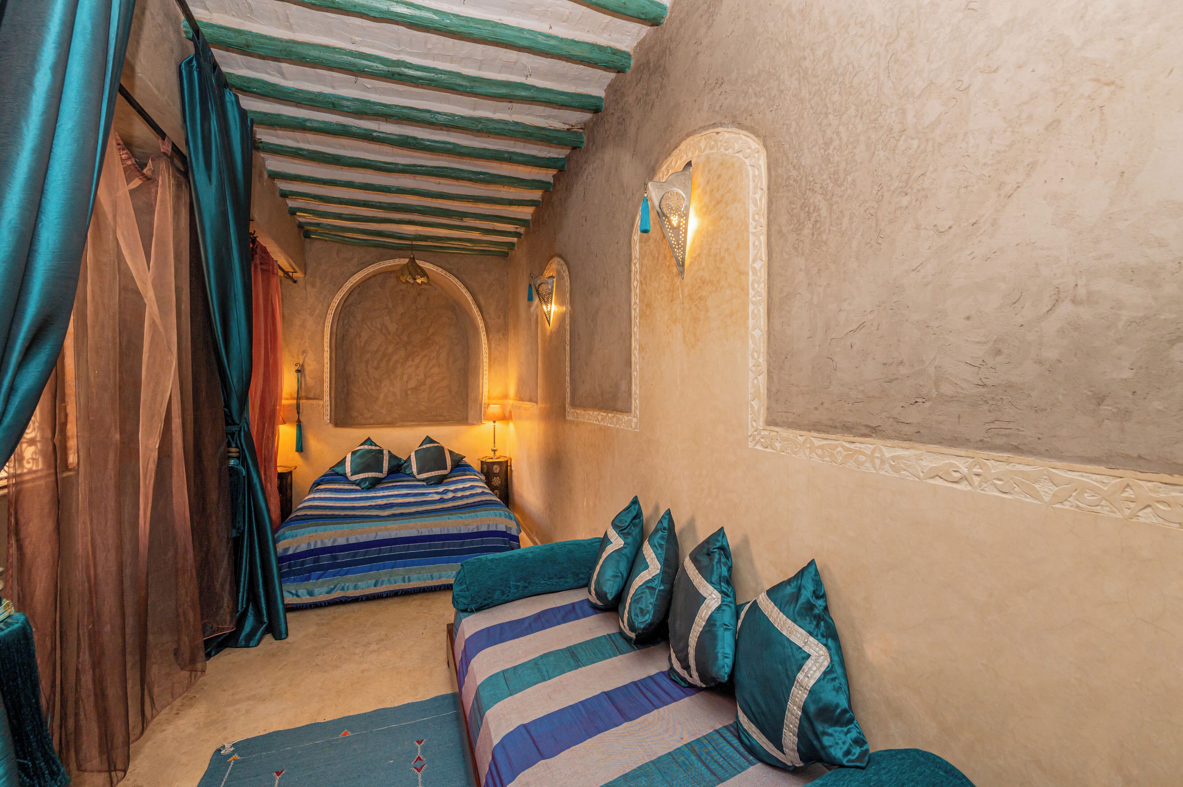 Une chambre avec deux lits, chacun doté de draps à rayures et d’oreillers assortis. Il y a une fenêtre avec un cadre décoratif et un luminaire fixé au mur.