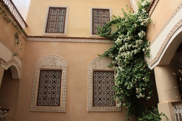 A building with ornate window designs and a climbing plant with white flowers.