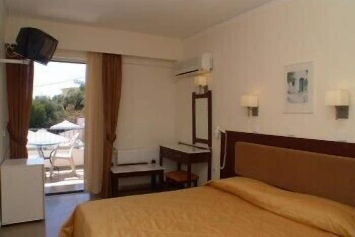 A hotel room with a bed, a desk, a chair, a mirror, and a window with curtains.