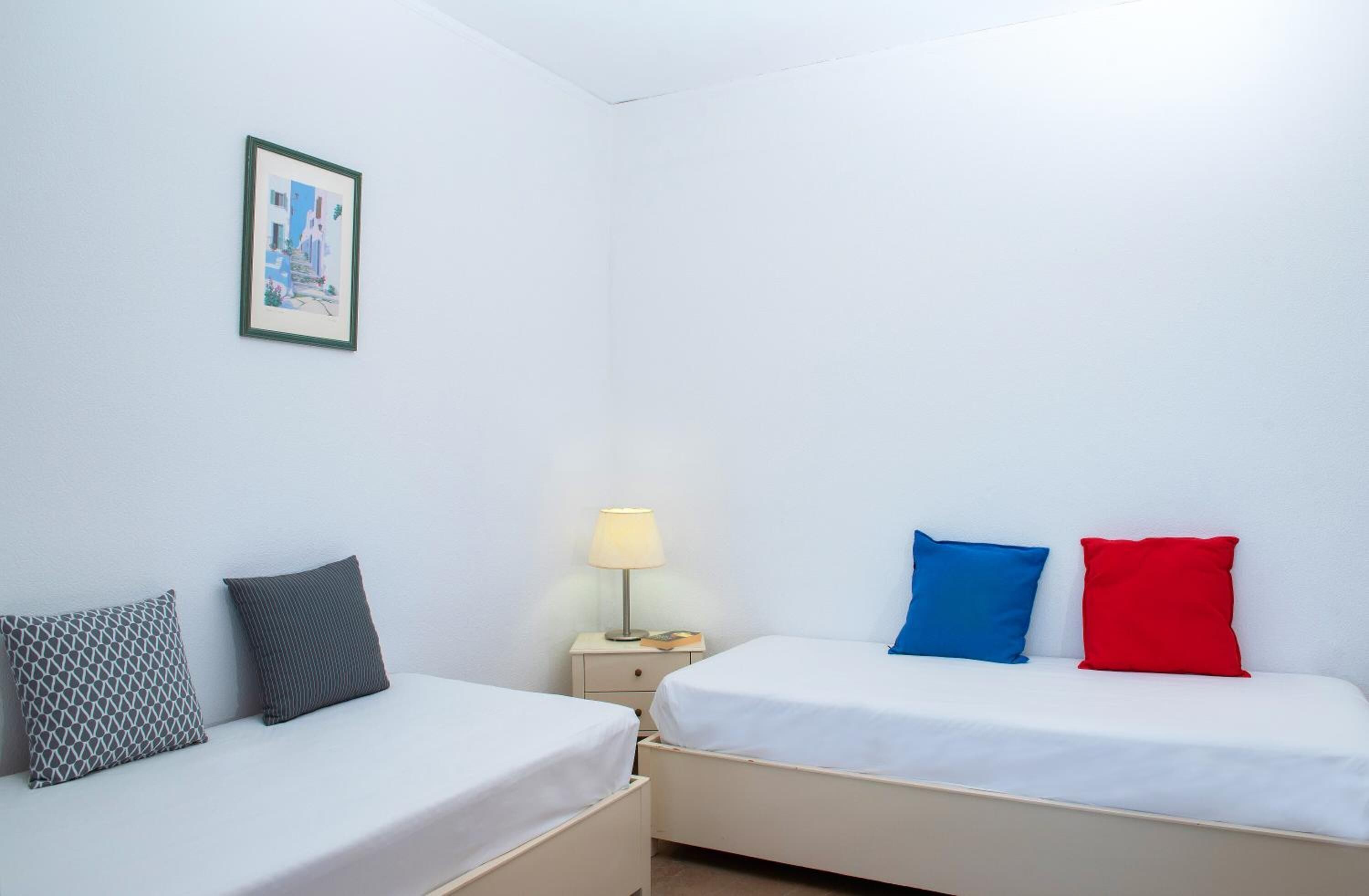 A room with two beds, each with a pillow and a bedside table with a lamp.