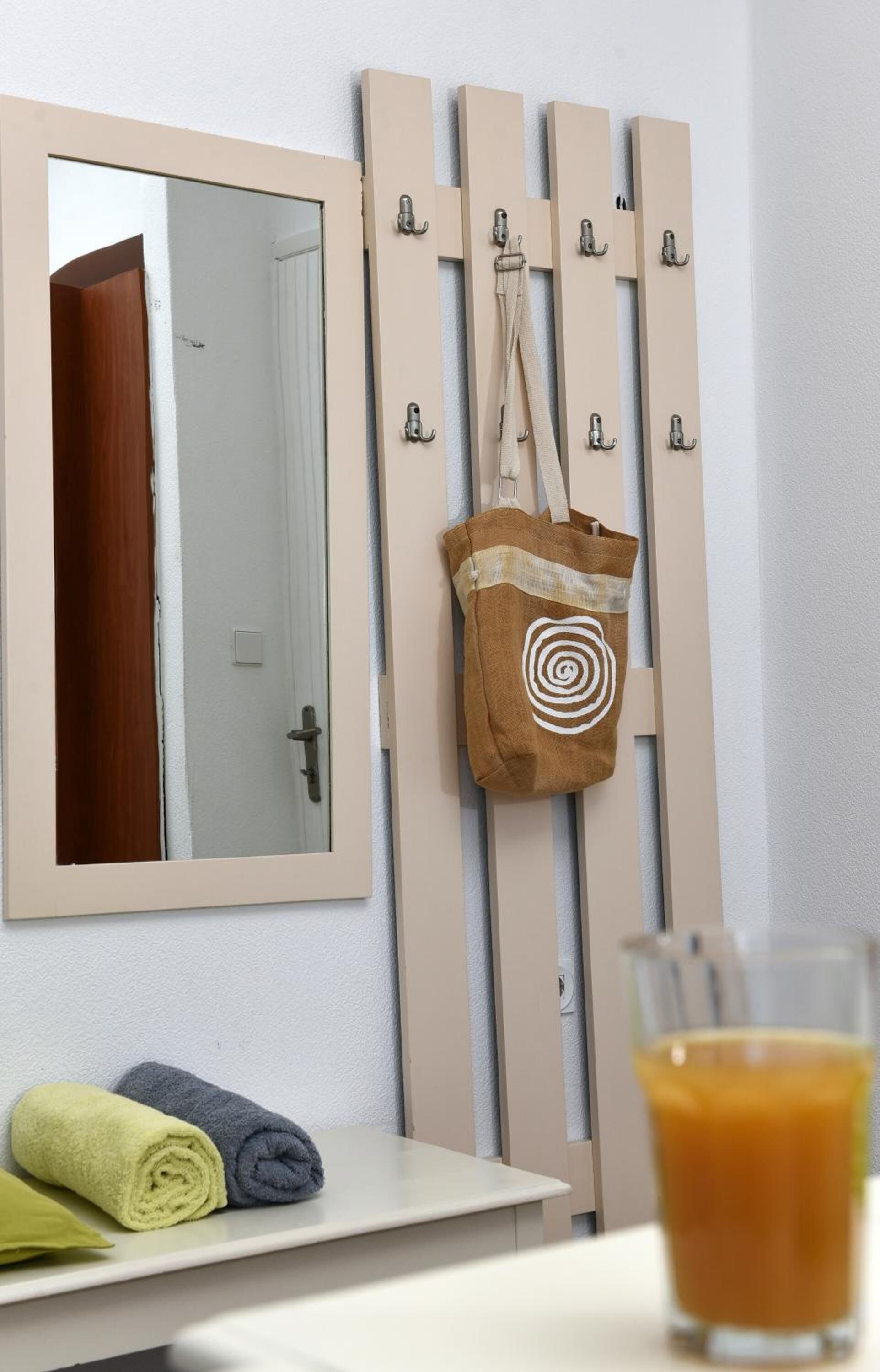 Un baño con espejo, toallero y un vaso de jugo de naranja sobre una mesa.