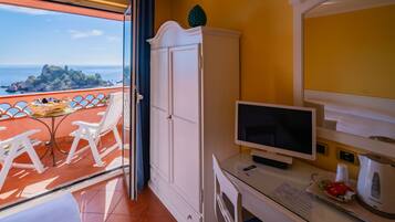 Una stanza con balcone, arredi bianchi, televisione, bollitore e vista sul mare.