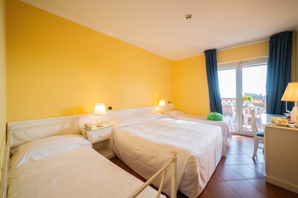 A hotel room with two beds, a desk, and a balcony with a view.