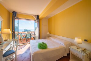 A hotel room with a bed, a desk, a chair, a nightstand, and a balcony with a view. - Mendolia Beach Hotel (Taormina)