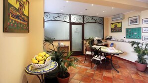 Un comedor con una mesa, sillas y una cesta de limones. Hay plantas en macetas y una pared con cuadros.