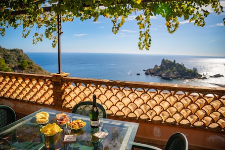 A table with a bottle of wine, glasses, and food on a terrace overlooking the sea.