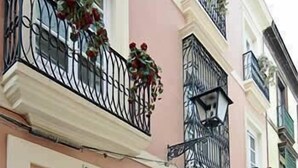Une façade d’immeuble avec une grande porte en bois, un balcon doté de balustrades en fer forgé noir et des plantes en pot.