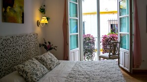 Une chambre avec un lit, une lampe fixée au mur et une vue sur l’extérieur, visible à travers une porte ouverte.