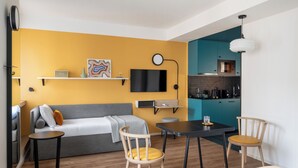 Un salón moderno con un sofá, una mesa de comedor y sillas, una zona de cocina y un televisor montado en la pared.