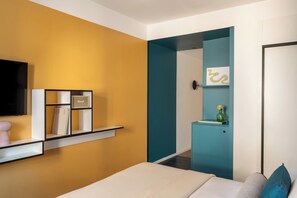 Un dormitorio con una cama, un televisor, una estantería con libros y un florero, y una pared de acento color aguamarina.