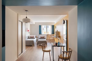 A modern hotel room with a bed, two chairs, a desk, and a large mirror.