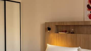 Une chambre d’hôtel avec un lit, des oreillers, une table de chevet, une étagère fixée au mur et un tableau encadré.