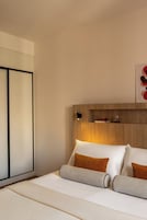 Camera d'albergo con un letto, cuscini, comodino, mensola a parete e una foto incorniciata.