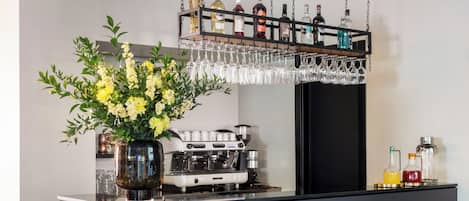 A modern bar area with a wooden counter, a coffee machine, and a vase of flowers.