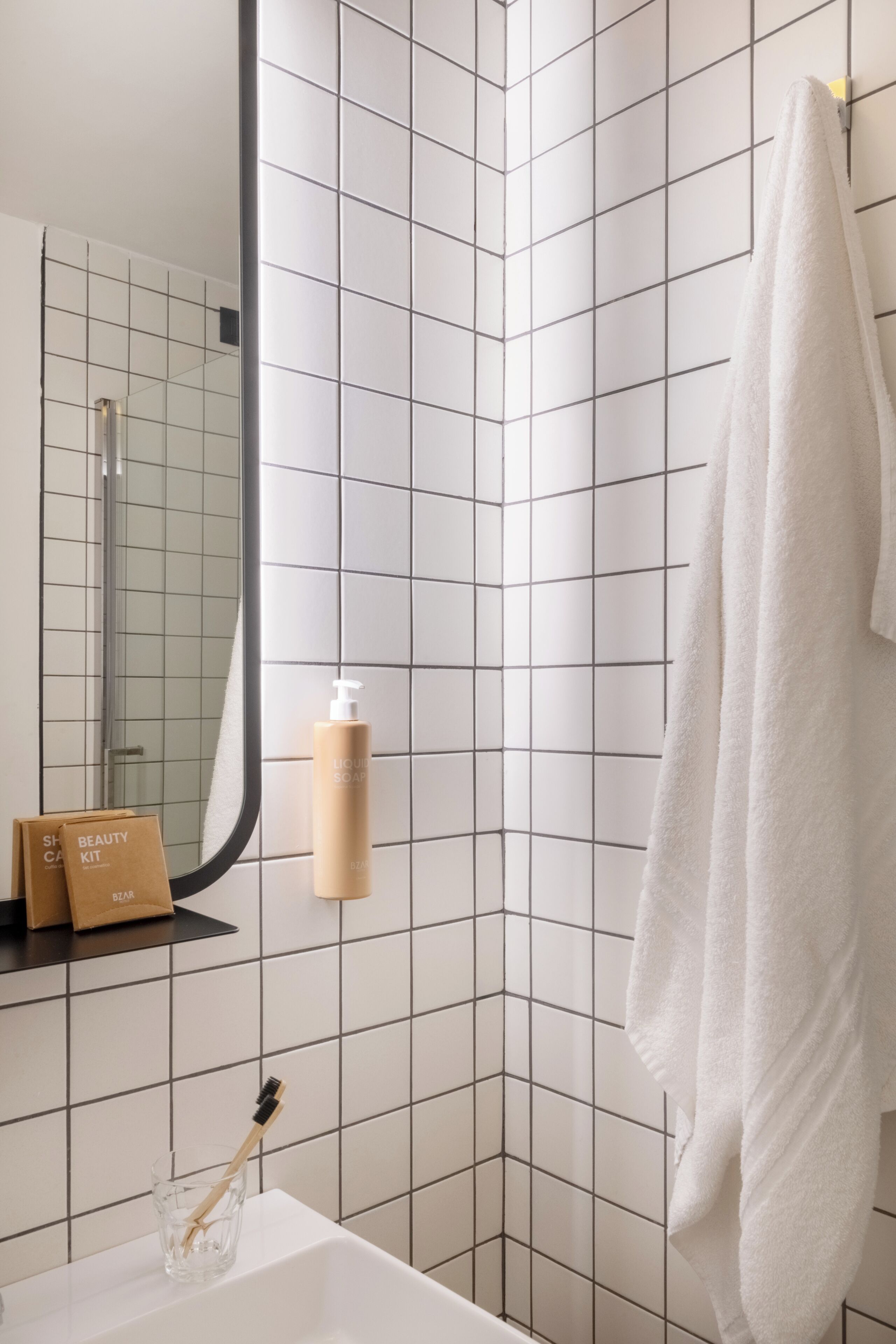 Un baño con un lavamanos blanco, un espejo, una toalla colgada en la pared y una botella de jabón líquido.