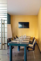 Una sala conferenze con un lungo tavolo, sedie, una lavagna e una televisione a schermo piatto appesa al muro.