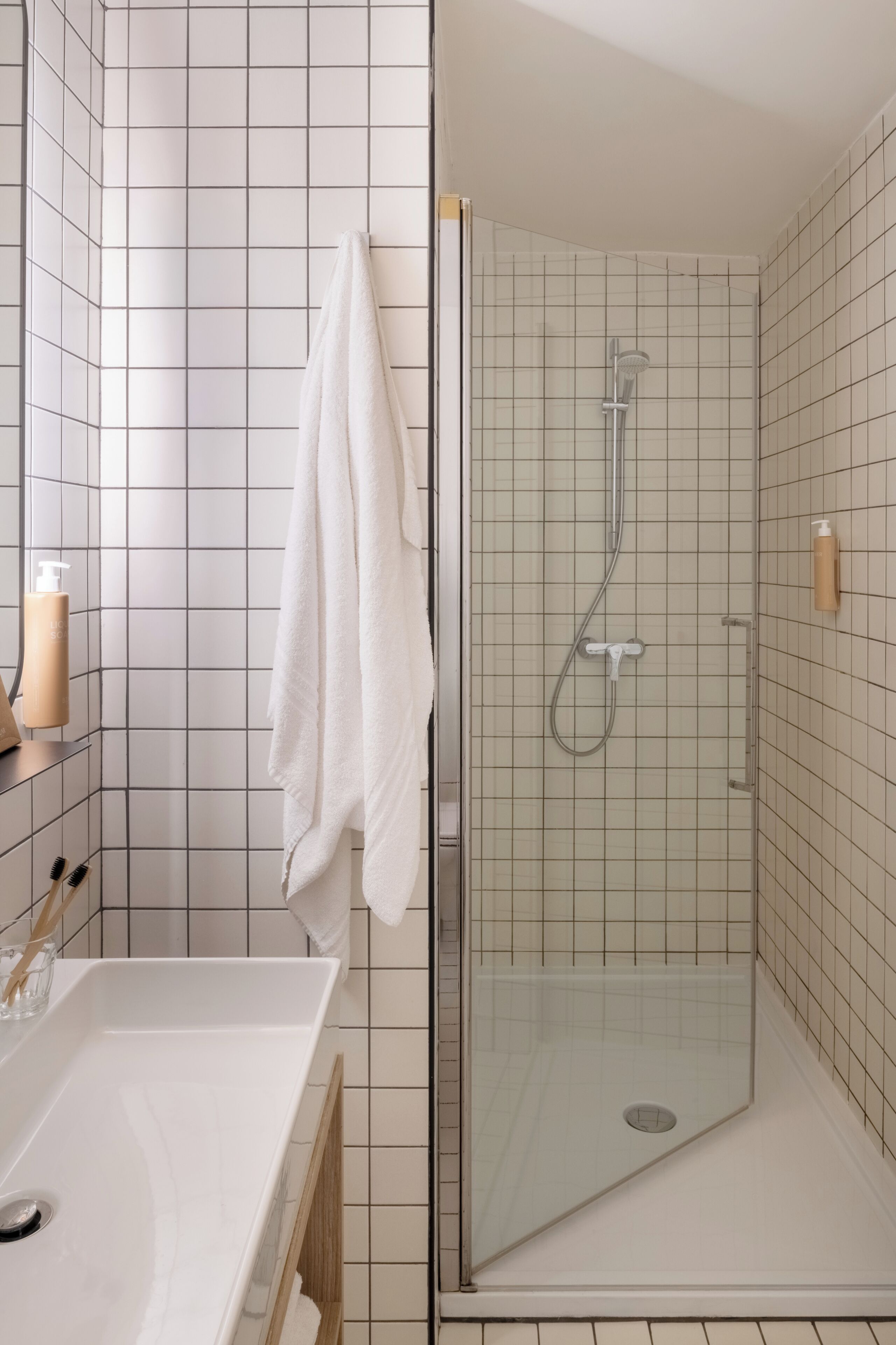 Een badkamer met een douche met glazen wand, een witte wastafel en een handdoek aan de muur.
