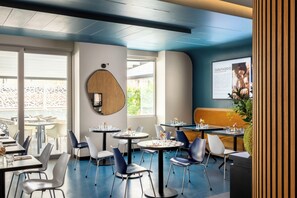 Un interior de restaurante moderno con mesas redondas, sillas y un ventanal grande.