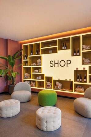 A shop area with multiple shelves displaying various items, including wine bottles and bags. There are seating areas with ottomans and a potted plant. - Aparthotel Colombo Roma (Rome)