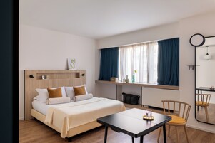 Una camera d'albergo con un letto, una scrivania, una sedia, una finestra con tende e uno specchio.