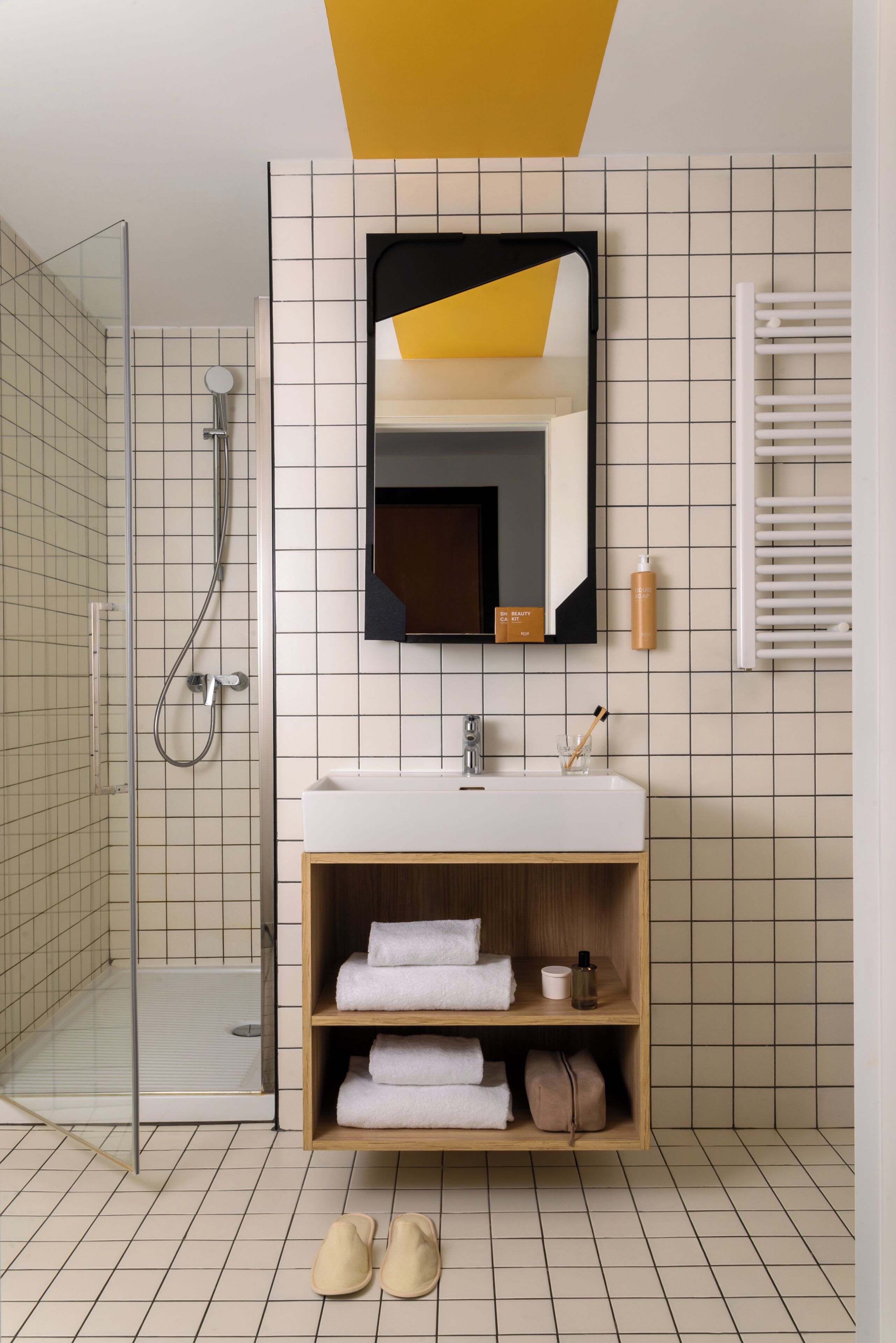 Un baño moderno con cabina de ducha de vidrio, un lavamanos blanco y un mueble de tocador de madera con toallas.