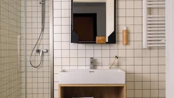Un baño moderno con cabina de ducha de vidrio, un lavamanos blanco y un mueble de tocador de madera con toallas.